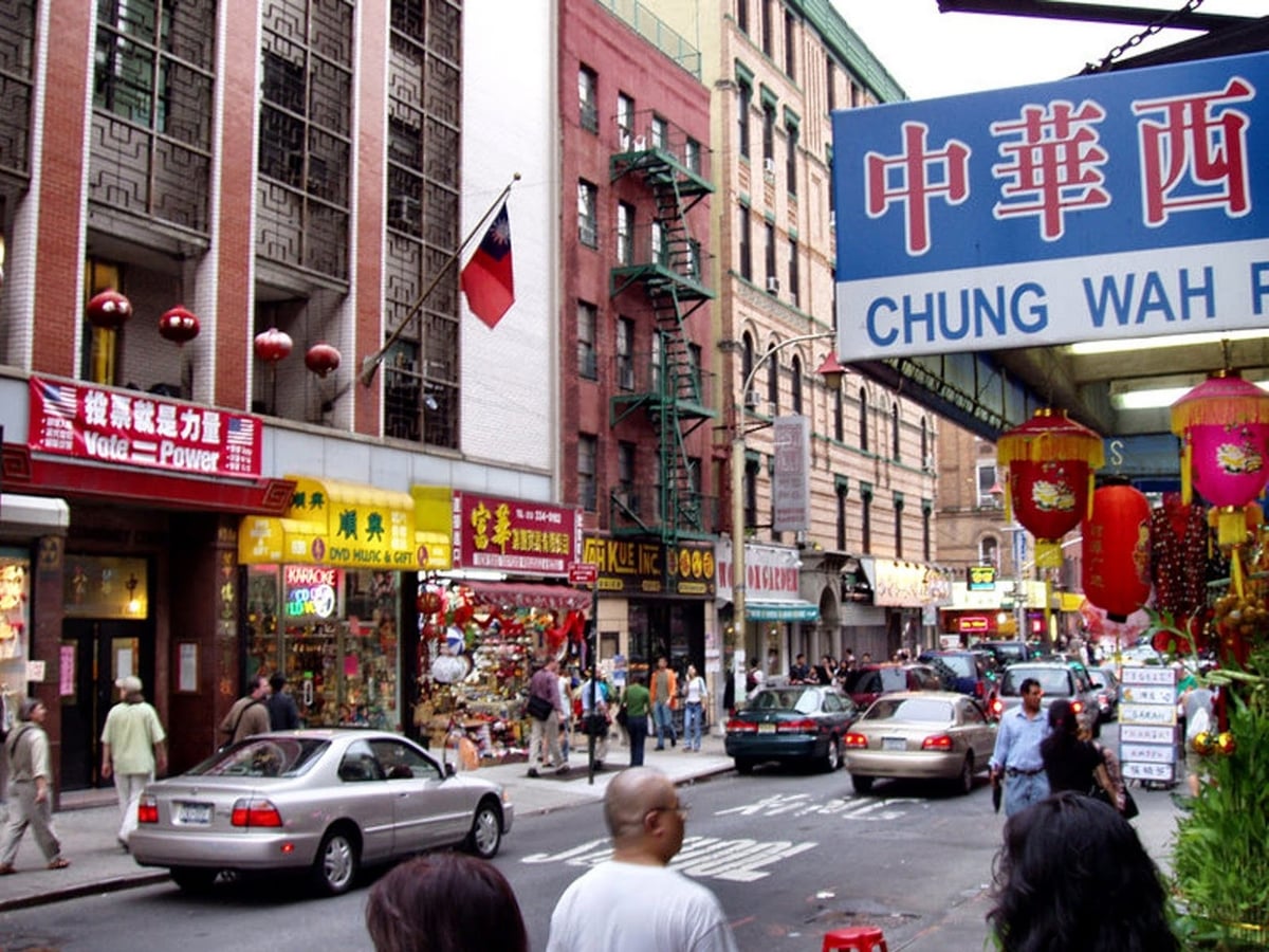 Una calle de Chinatown en Nueva York con rótulos en caracteres chinos y farolas rojas colgando sobre las tiendas y los puestos callejeros.