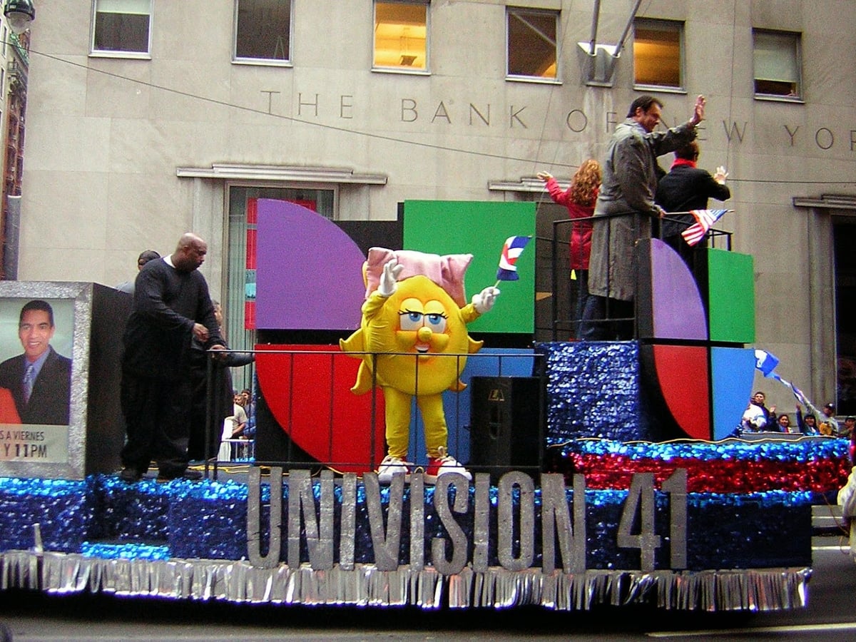 Una carroza del Desfile de la Hispanidad avanzando por la Quinta Avenida, decorada con banderas y motivos de países latinoamericanos, rodeada de espectadores en las aceras.