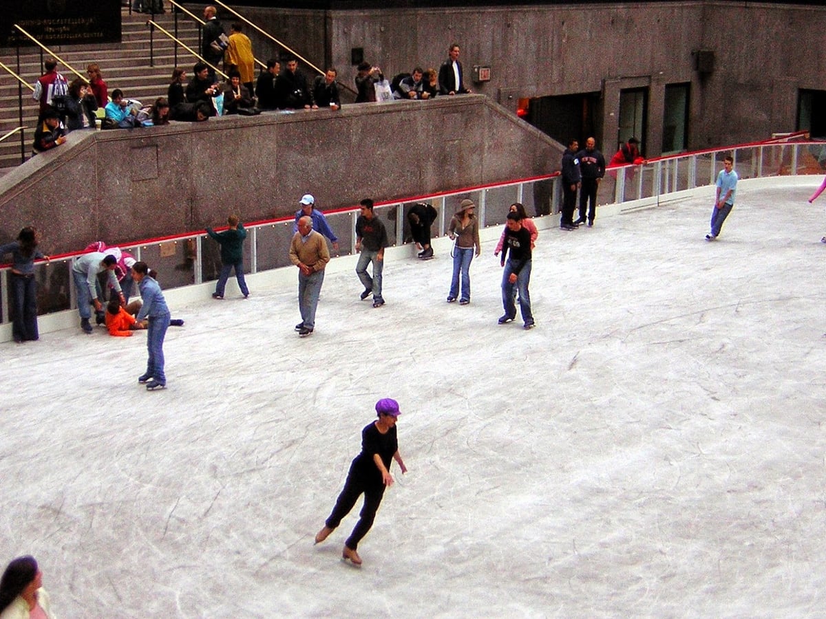 Vista general de la pista de hielo del Rockefeller Center, con las banderas de distintos países en el perímetro y la estatua dorada de Prometeo al fondo.