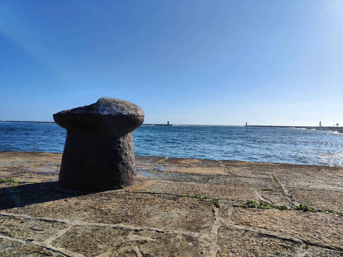 El Farol de Felgueiras, pequeño faro rojo sobre el rompeolas de piedra en la desembocadura del Duero, con una ola del Atlántico rompiendo contra la base.