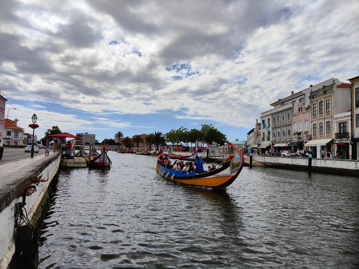Moliceiros de proa alzada y popas pintadas con colores vivos amarrados en el Canal Central de Aveiro, con las fachadas del centro reflejándose en el agua.