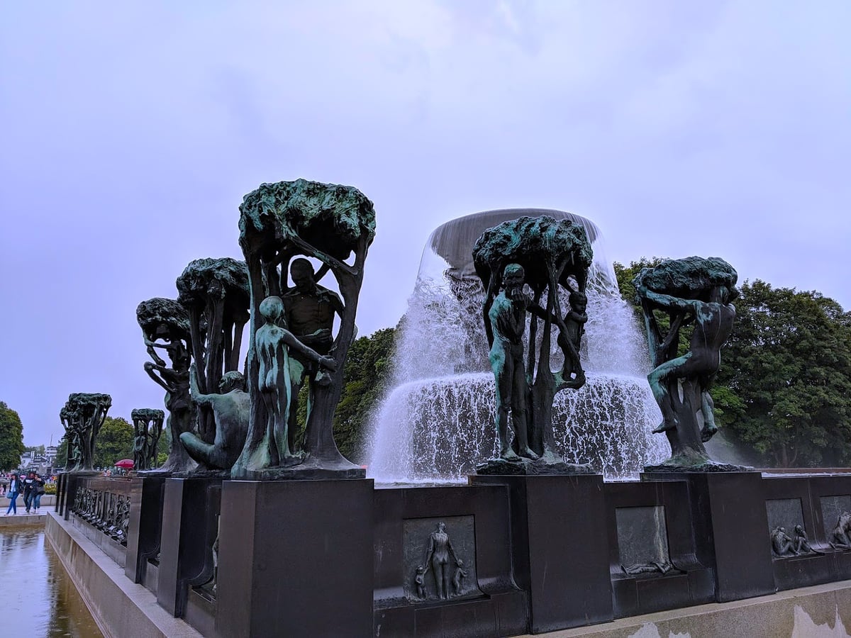 La Fuente del parque Vigeland, con figuras de bronce entrelazadas entre árboles estilizados bajo un cielo cubierto