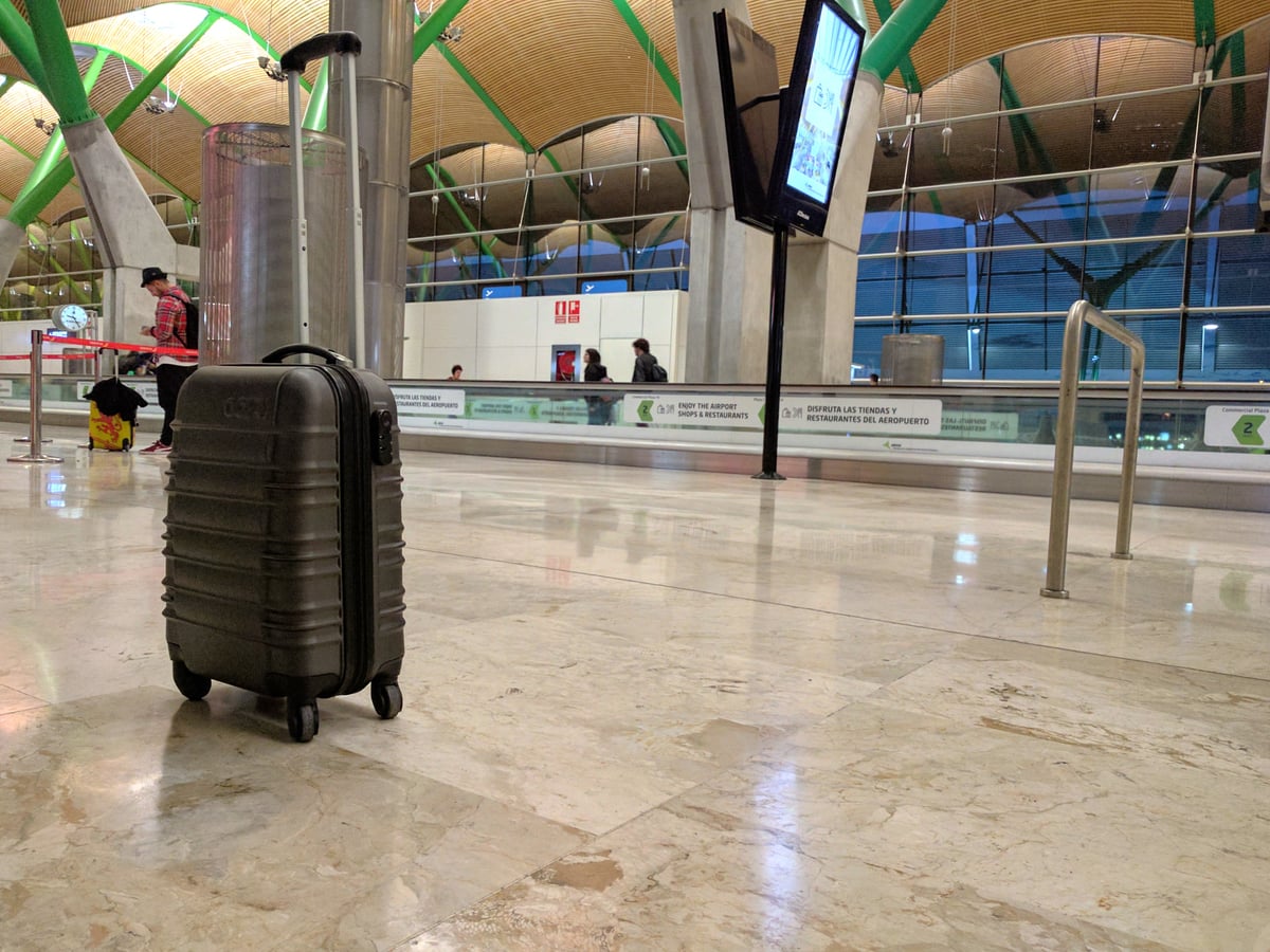 Una maleta de cabina gris con ruedas, sola en medio del suelo de mármol de la terminal T4 de Barajas, bajo la cubierta ondulada de bambú y los pilares en forma de Y.