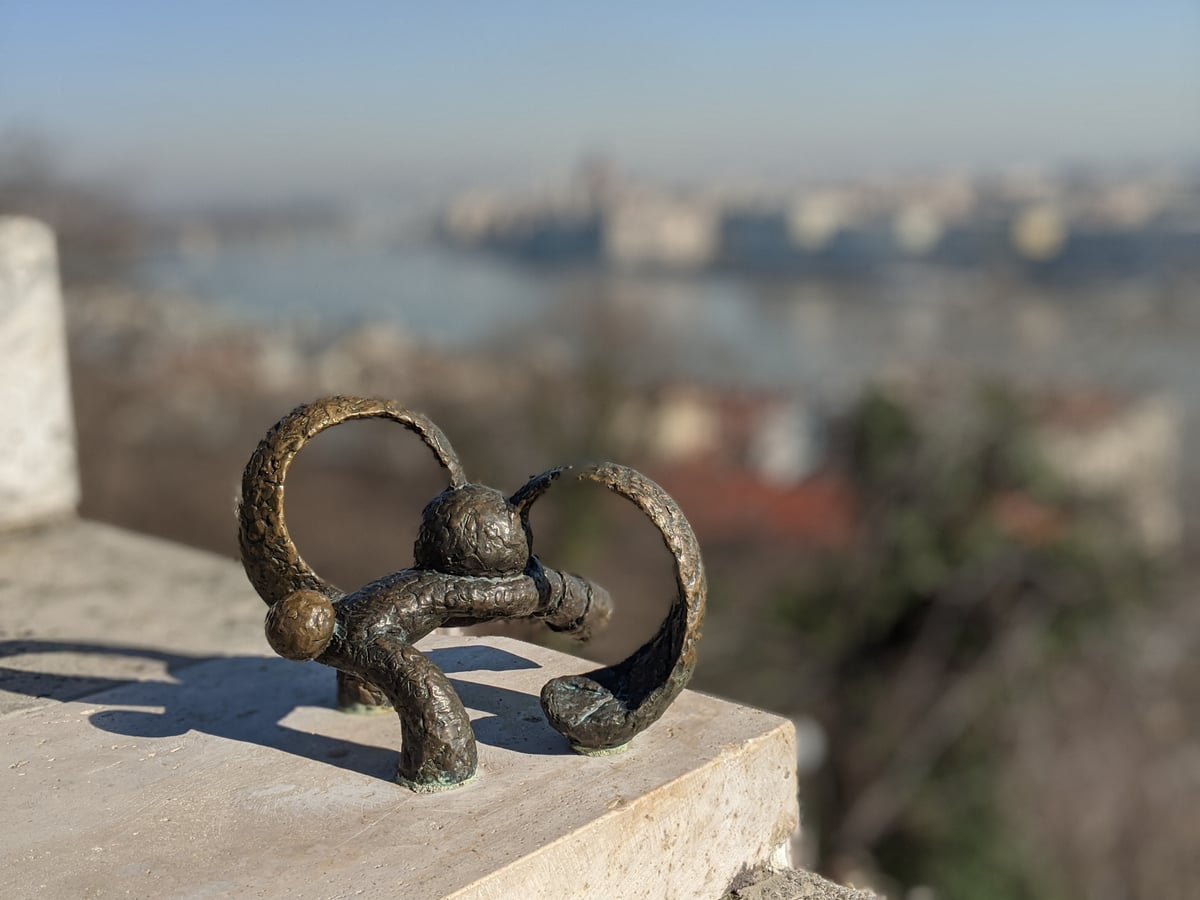 Miniatura de bronce de un animal de orejas enormes y redondas, apenas del tamaño de una mano, colocada en el pretil de piedra de un mirador con el río y los tejados de la ciudad desenfocados detrás.