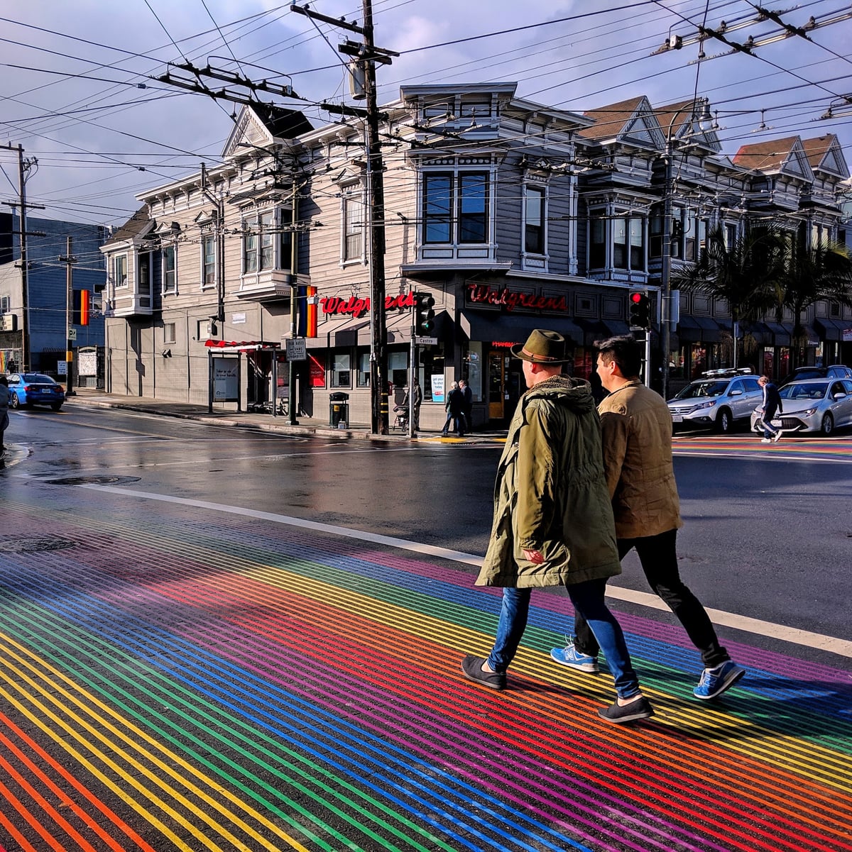 Dos hombres cruzan cogidos de la mano un paso de cebra pintado con los colores de la bandera LGTBI en el barrio de Castro, en San Francisco.