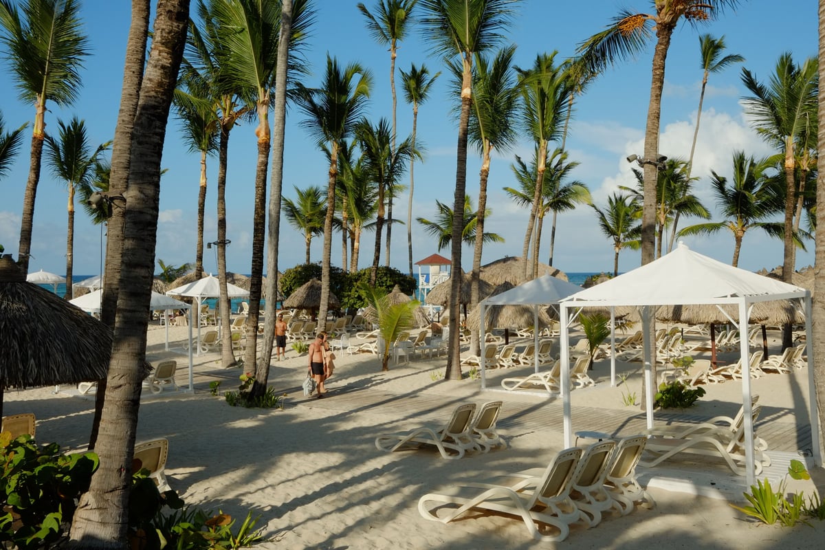 Escena idílica de playa tropical con palmeras, tumbonas y sombrillas en un resort frente al mar.