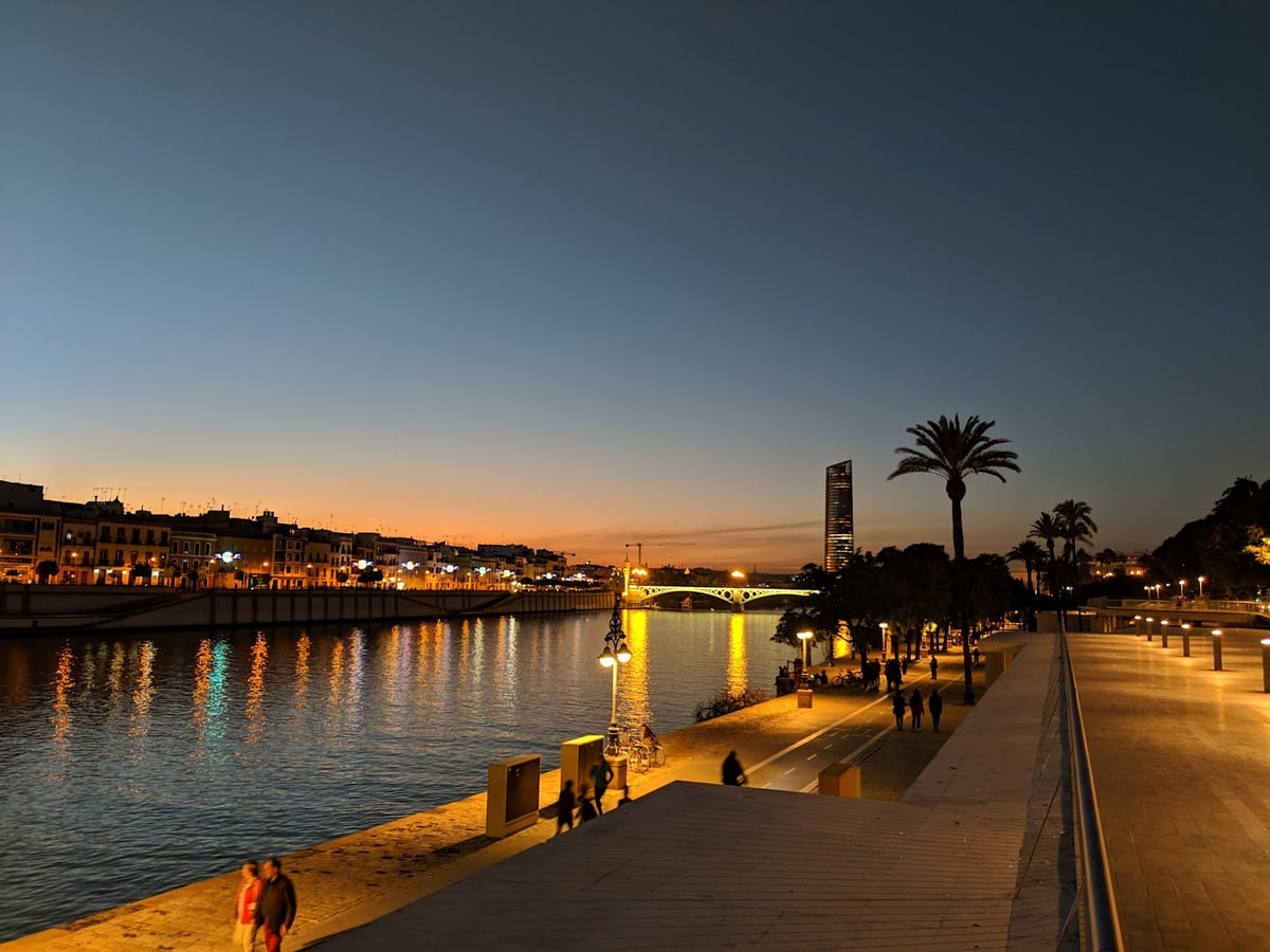 El paseo junto al Guadalquivir en Triana al anochecer, con el puente y la Torre Sevilla iluminados al fondo