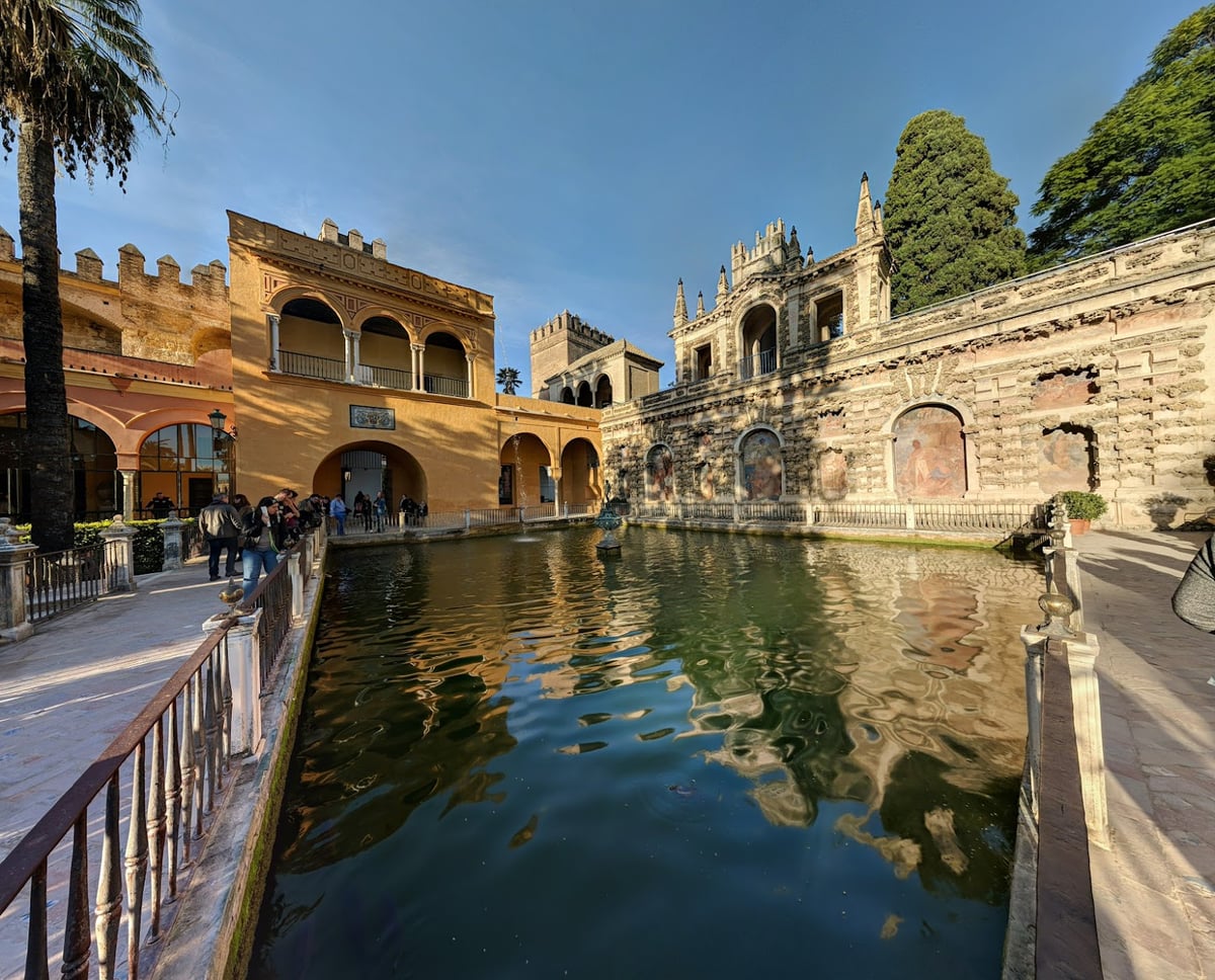El estanque de un patio del Real Alcázar, con la fachada dorada del palacio y sus torres reflejadas en el agua