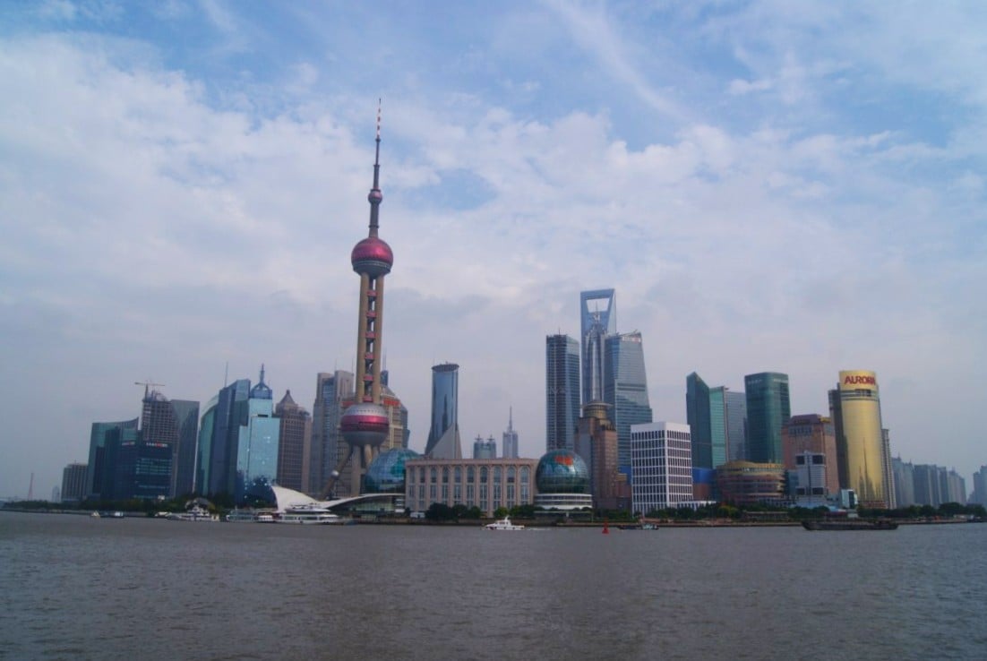 El skyline de Pudong visto desde el otro lado del río Huangpu, con la torre de la Perla Oriental y sus esferas rosas en el centro, rodeada de rascacielos y con el agua parda del río en primer plano.