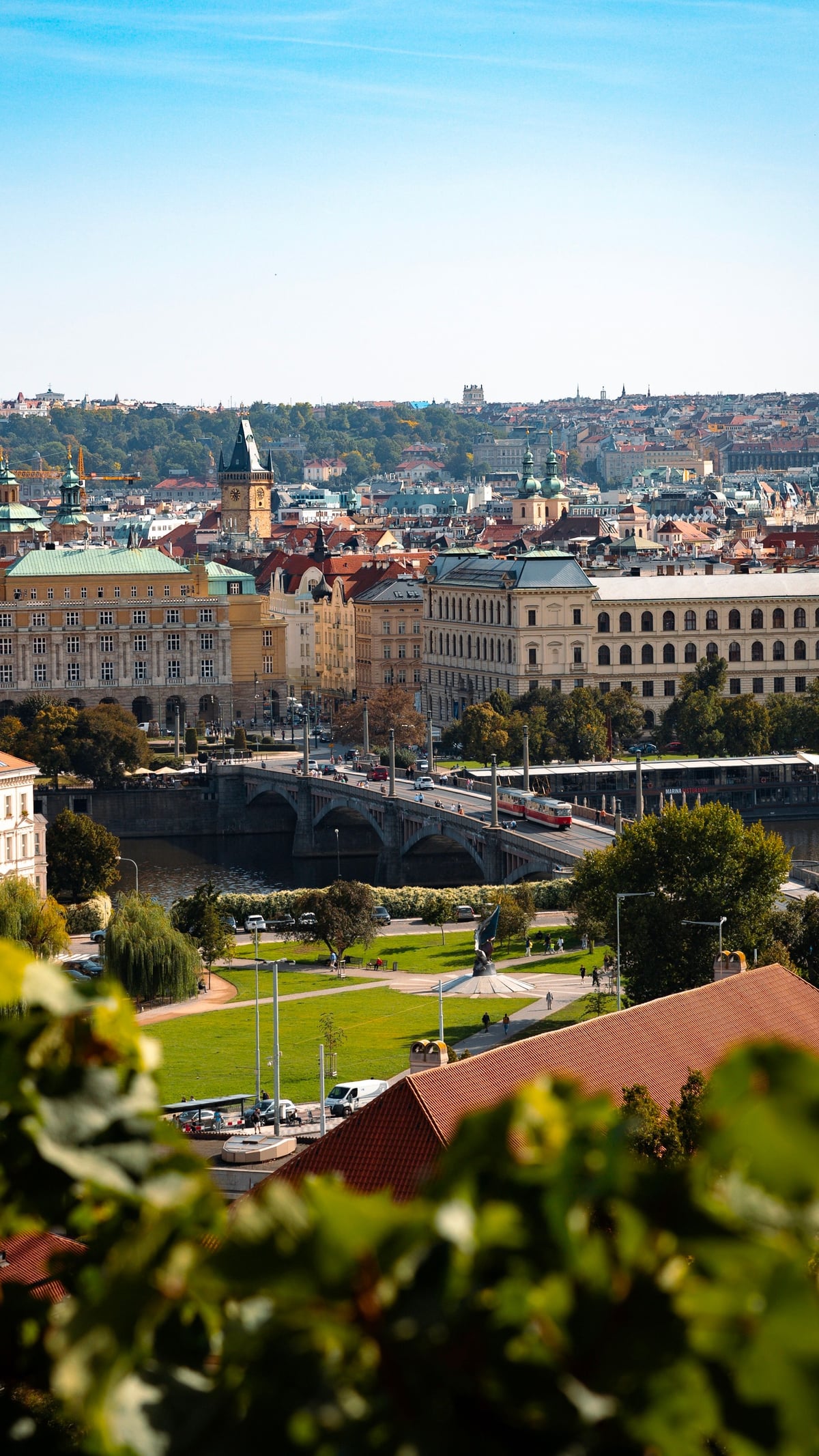 Vista aérea escénica de Praga que muestra arquitectura histórica, un puente y parques exuberantes.