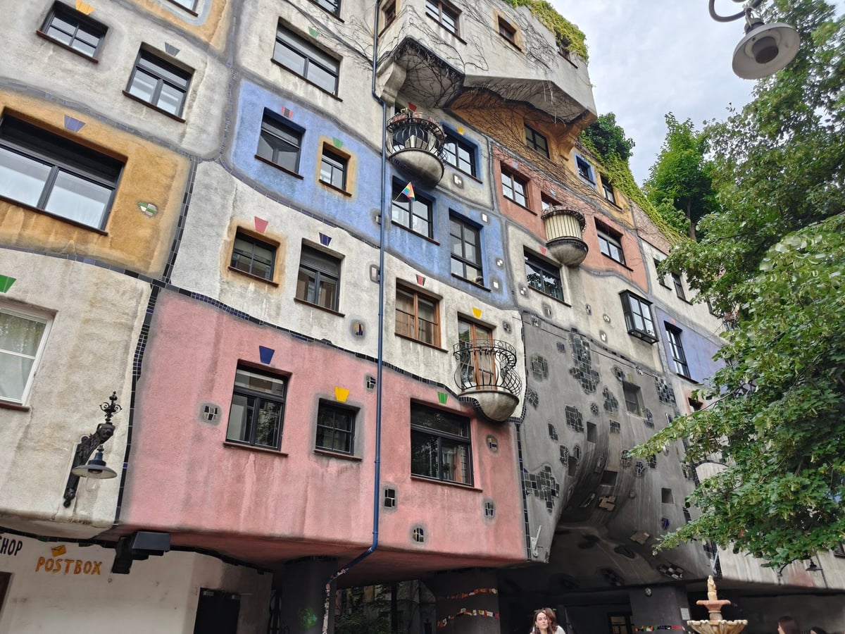 La fachada ondulada y policromada de Hundertwasserhaus en Viena, con balcones irregulares cubiertos de vegetación y ventanas de formas y tamaños distintos.