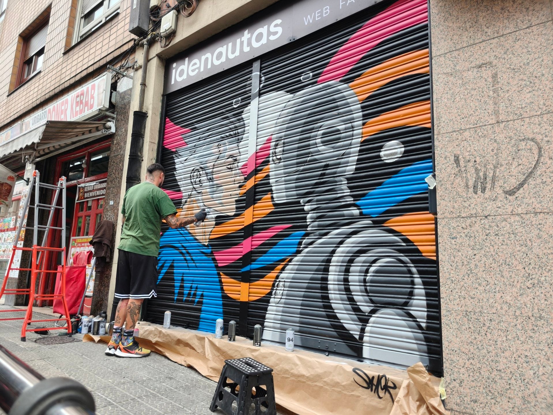 Okiman pintando con spray el diseño del mural en la persiana de Idenautas